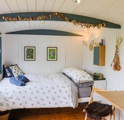 A bedroom with a bed with patterned bedding next to a window and a wooden desk with a chair at Oak Shepherd Hut Monkton Wyld near Charmouth