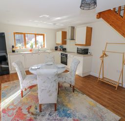 A kitchen and dining area with a round glass table and four chairs on a multicolored rug at Little Barn in Dodwell near Stratford-Upon-Avon