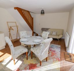 A dining area with a round table set with plates and glasses surrounded by four floral chairs near a wooden staircase and a beige sofa at Little Barn Dodwell near Stratford-Upon-Avon