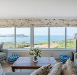A living room with sofas pillows table lamp and flowers with a sea view at Splits in Daymer Bay
