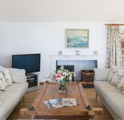 A living room with two sofas facing a wooden coffee table with flowers and magazines at Splits in Daymer Bay