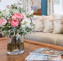 A bouquet of flowers in a glass vase on a wooden coffee table with magazines in a living room at Splits in Daymer Bay