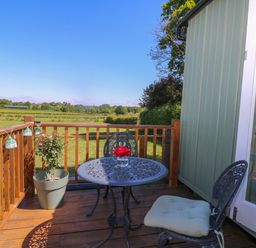 A wooden deck with a metal table and two chairs overlooking a green field at Songbirds in St Michaels Kent
