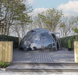 A transparent geodesic dome on a wooden deck surrounded by hedges and trees at Number 1 Dome in Derrybeg County Donegal
