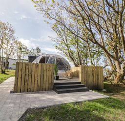 A clear dome structure on a wooden deck with steps surrounded by wooden fence and trees at Number 2 Dome in Derrybeg County Donegal