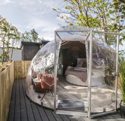 A transparent geodesic dome with a bed and chairs inside on a wooden deck surrounded by a wooden fence at Number 2 Dome in Derrybeg County Donegal