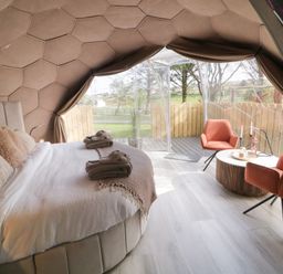 A bedroom with a bed, two orange chairs, a round table, and large windows at Number 2 Dome in Derrybeg County Donegal