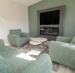 A sitting room with green upholstered chairs sofas a rug coffee tables a mounted television and fireplace at Number 2 Villa - The View in Derrybeg County Donegal