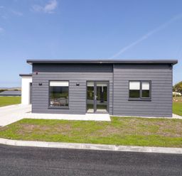 A modern single story house with grey cladding windows and a door surrounded by grass and paved driveway at Number 2 Villa - The View in Derrybeg County Donegal