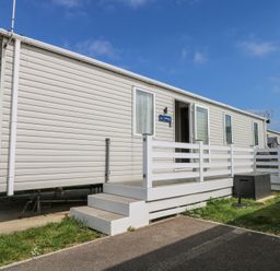 A mobile home with white siding and a small porch with steps on a grassy lot at HW42 in Bognor Regis