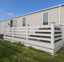 A mobile home with white railings and outdoor seating on a wooden deck at HW42 in Bognor Regis
