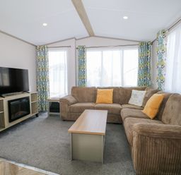 A living room with a brown sectional sofa yellow cushions a wooden coffee table a TV on a stand and floral curtains at HW42 in Bognor Regis