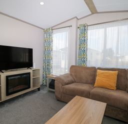 A living room with a brown sofa yellow pillow TV on wooden cabinet and floral curtains at HW42 in Bognor Regis
