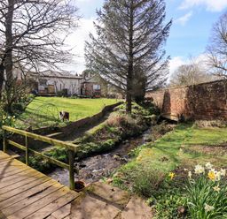 A garden with a bridge over a stream and a dog at Yew Tree Cottage in Mealsgate near Ireby