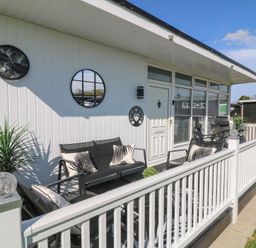 A patio with outdoor seating and cushions next to a white paneled building at 56 Cherry Park Chalet in Chapel St Leonards