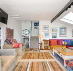 A living room with a striped carpet a wooden coffee table a colorful sectional sofa and framed pictures on the walls at 5 Esplanade in Fowey