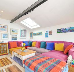 A living room with a large sectional sofa with colorful cushions and a wooden coffee table under a skylight at 5 Esplanade in Fowey