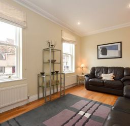 A living room with black leather sofas glass shelving and large windows at Churchside in Alnwick