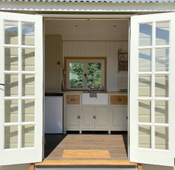 A kitchen with a farmhouse sink visible through open double glass doors at Shepherd Hut 1 in Northchapel
