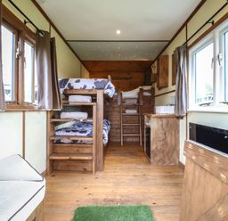 A small bedroom with bunk beds, wooden floor, windows with curtains, and a small desk at Buttercup (Cow Shed 3) in Easton near Campsea Ashe