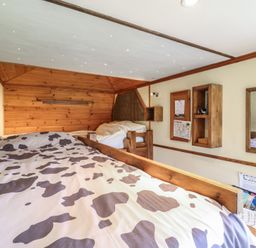 A small bedroom with two wooden beds one with cow print bedding and wooden shelves on the wall at Buttercup Cow Shed 3 in Easton near Campsea Ashe
