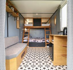 A room with bunk beds a bench a wooden cabinet with a kettle and a window with curtains at Dozy Dotty Cow Shed 4 in Easton near Campsea Ashe