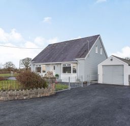 A detached house with a steep roof and an adjacent garage with a paved driveway and a fenced front garden at Bryn Derw in Caernarfon