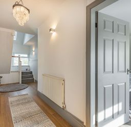 A hallway with wooden floor rugs a grey door and stairs leading up at Bryn Derw in Caernarfon