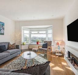 A living room with gray sofas a coffee table armchair bay window and a wall-mounted television at Bryn Derw in Caernarfon