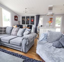 A living area with grey sofas pillows a kitchen island with flowers and a dining table with chairs at 155 Woodland Hall Lyons Ruthin