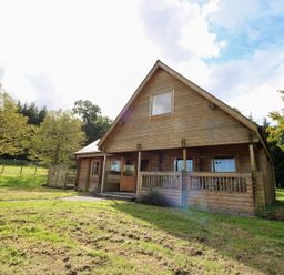 A wooden house with a veranda and surrounding trees at Dan Y Coed near Beggar's Bush near Presteigne
