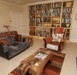 A living room with a bookshelf, sofa, and chair at Elford Farmhouse in Seahouses