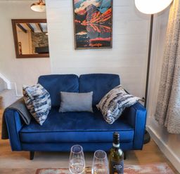 A blue sofa with cushions in a living room with a bottle of wine and glasses on a wooden floor at 4 Old Tanrhiw in Beddgelert