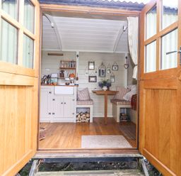 A small kitchen and dining area with wooden floors and open double doors at Sika in Warmwell