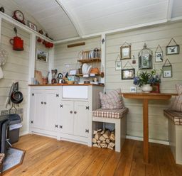 A small kitchen and dining area with wooden floor cabinets dishes and a wood stove at Sika in Warmwell