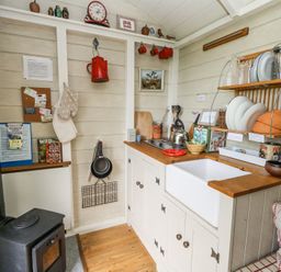 A small kitchen with a wood stove and sink with dishes on a rack at Sika in Warmwell