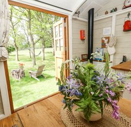 An indoor dining area with a flower vase on the table wooden floor and view of a garden with trees and a wooden chair at Sika in Warmwell