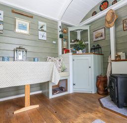 A small dining area with a table and bench seating next to a black wood stove and cabinets at Fallow in Warmwell