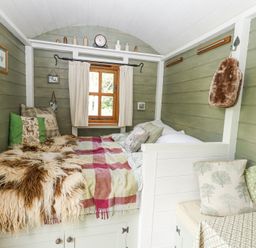 A small room with a bed covered by throws and pillows near a window with curtains and green wooden walls at Fallow in Warmwell