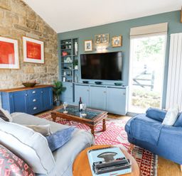 A living room with blue armchair a sofa a wooden coffee table a blue cabinet and a television at The Barn in Riding Mill near Corbridge