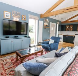 A living room with a sofa, blue armchair, coffee table, large TV on a blue cabinet, and open kitchen at The Barn in Riding Mill near Corbridge