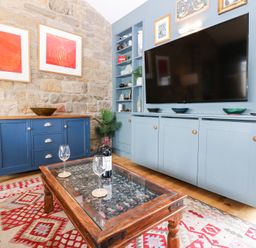 A living room with a TV on a blue cabinet a wooden coffee table with wine glasses and a bottle and a blue sideboard against a stone wall at The Barn in Riding Mill near Corbridge