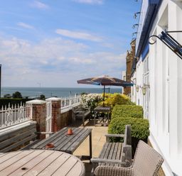 An outdoor patio with tables benches chairs umbrella and plants overlooking the sea at The Burleigh in Hunstanton