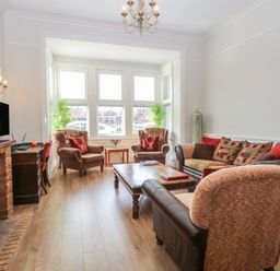 A living room with two armchairs, a sofa, a coffee table, a fireplace, and a desk by the window at The Burleigh in Hunstanton