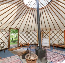 The interior of a yurt with a wood stove in the center rugs on the floor a wooden chair and a table with lanterns at Moonlight in Ventnor