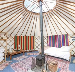 Interior of a yurt with a bed a stove rugs a wooden shelf and colorful wall hangings at Moonlight in Ventnor