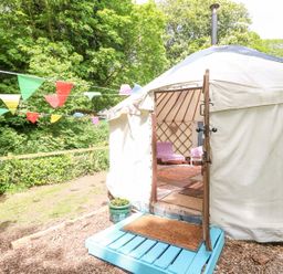 A round tent with an open door showing chairs and rugs inside and colorful bunting outside at Stardust in Ventnor