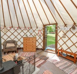 Interior of a yurt with a wood stove armchair wooden dresser rugs on the floor and a door open to grass outside at Stardust in Ventnor