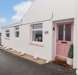 An exterior view of a house with a pink door and numbered sign at Penwyn in Solva