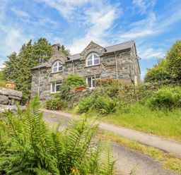 A stone cottage with arched windows surrounded by plants and trees at Dwynant in Bontddu near Dolgellau